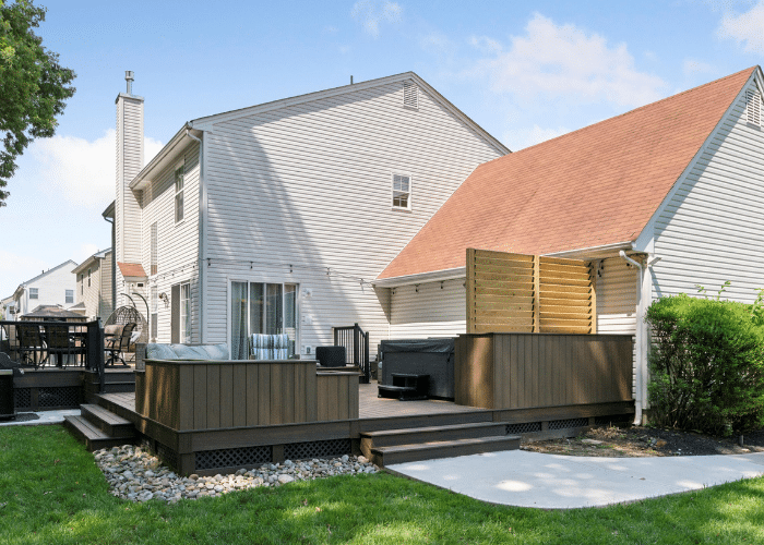 Completed deck project featuring Trex Enhance decking with white railings and black balusters, a covered seating area with a ceiling fan, and lattice skirting for a finished look. The deck is attached to a white house and overlooks a landscaped backyard