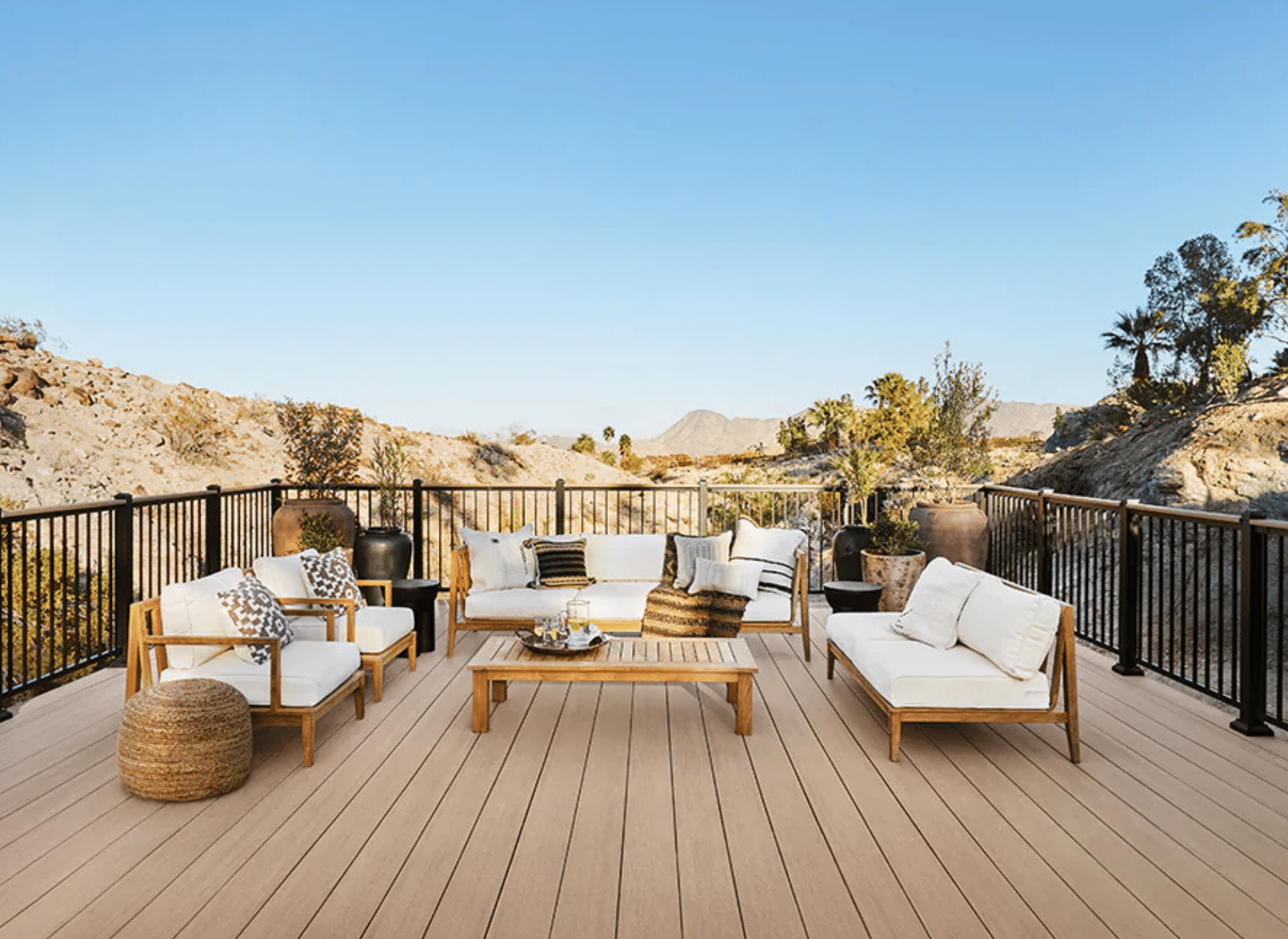 A spacious outdoor deck featuring light wood-tone PVC decking, black metal railings, and modern outdoor furniture, designed by a professional deck contractor in Upper Dublin, PA. (40.1533° N, 75.1896° W)