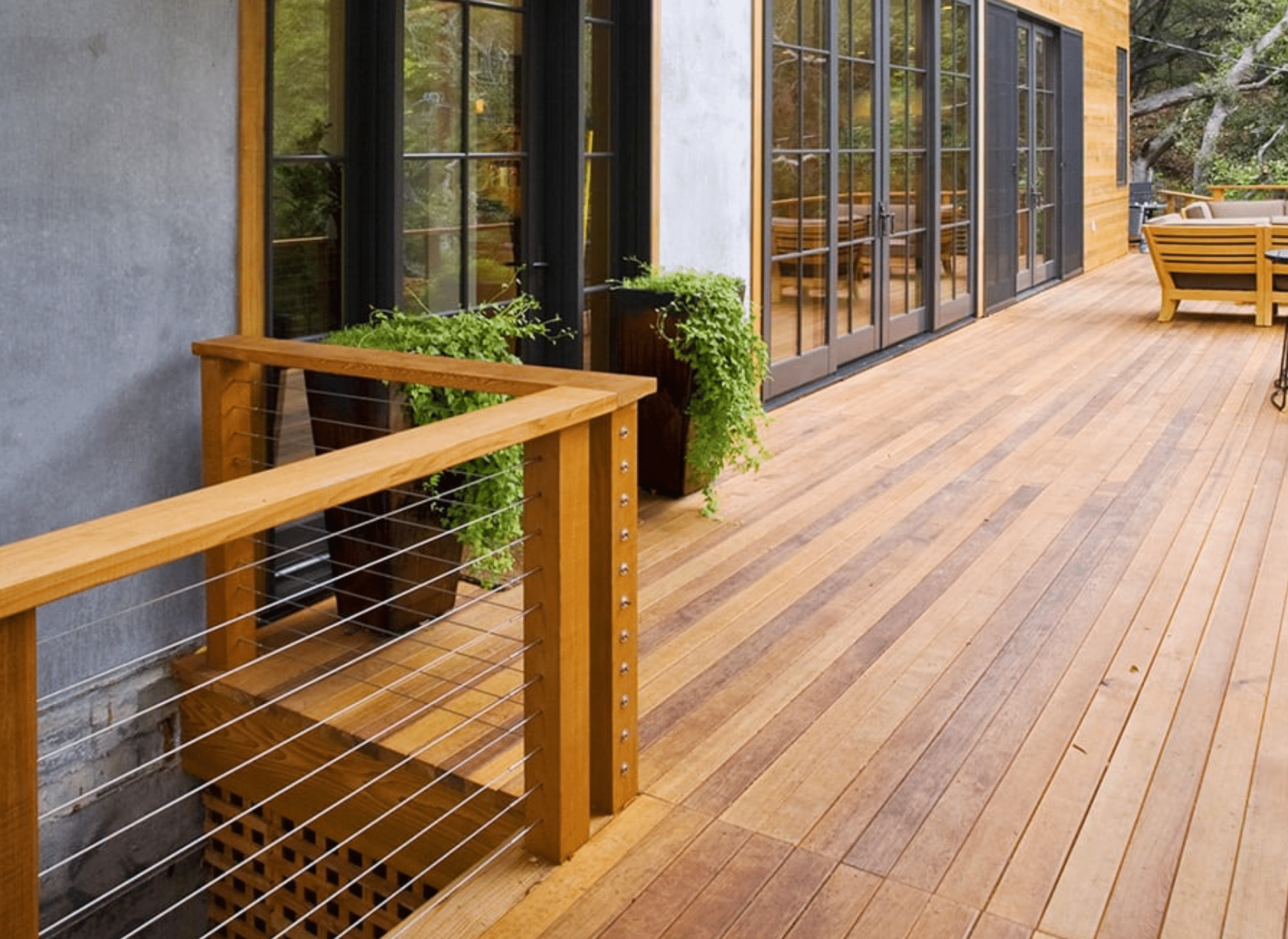 A custom cedar deck with sleek cable railings and large glass doors, extending from a modern home. The deck features warm wood tones, potted greenery, and an inviting outdoor dining area, built by a professional deck contractor in Glenside, PA. (40.0999° N, 75.1528° W)