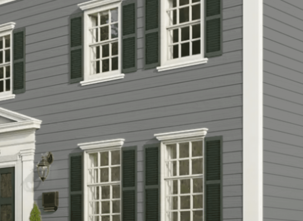 A traditional-style home featuring smooth gray HardiePlank® siding with a sleek, horizontal lap design. The exterior is accented by crisp white trim around the windows and corners, along with dark green shutters that add a classic touch. A decorative lantern and mailbox are mounted near the entrance, enhancing the home's elegant curb appeal.
