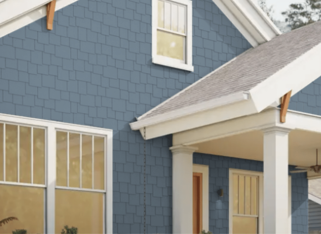 A craftsman-style home featuring deep blue Hardie® Shingle Siding with a staggered edge design. The siding is complemented by crisp white trim around the windows, doors, and roofline. The front porch has classic columns and a wooden front door, adding to the home's charm and durability.