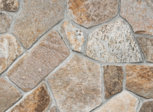 A close-up view of a mosaic stone veneer wall featuring irregularly shaped natural stones in earthy tones of brown, beige, and gray, fitted together with visible mortar lines.