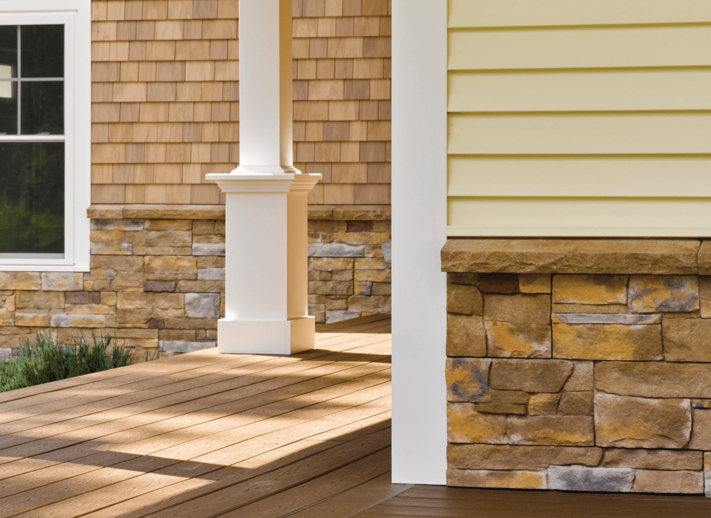 A close-up of a home's exterior featuring CertainTeed vinyl siding in soft yellow and cedar shake textures, complemented by a stone veneer base. White trim and a wooden porch add to the modern siding design.