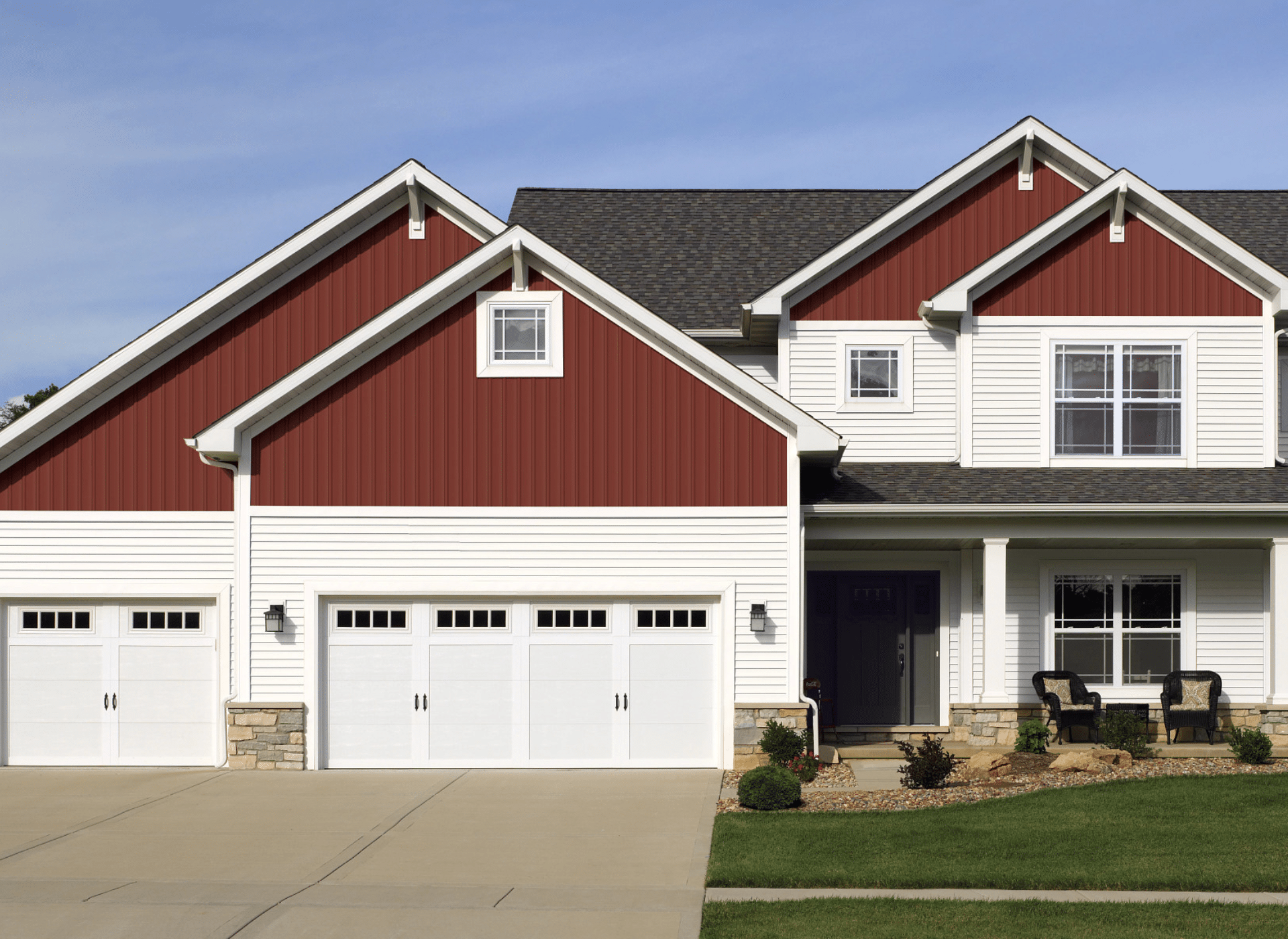 A modern farmhouse-style home featuring newly installed CertainTeed board and batten siding in red, paired with white horizontal siding. The house includes a three-car garage, a covered porch with seating, and well-manicured landscaping.
